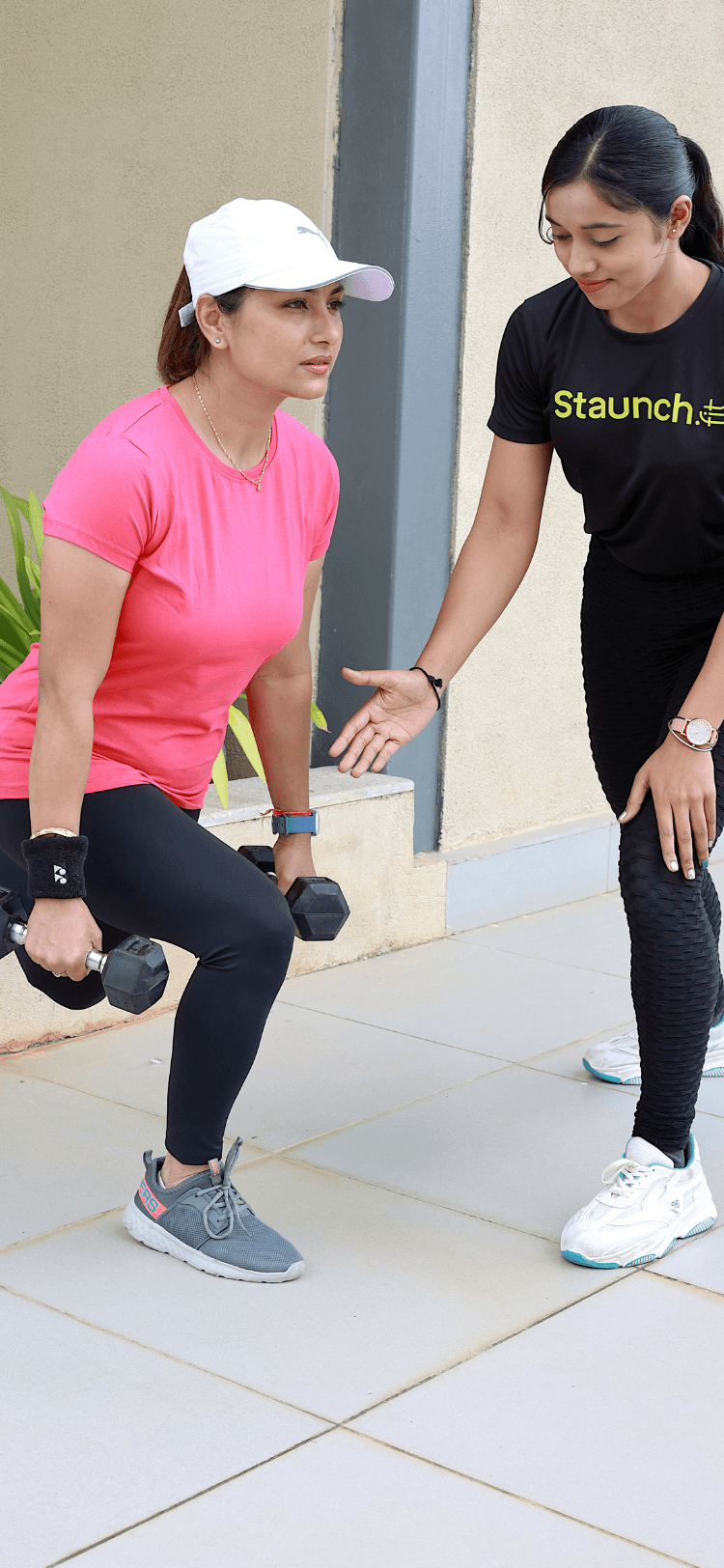 A Staunch trainer in branded tee coaching a resident through a dumbbell squat on an apartment-community terrace